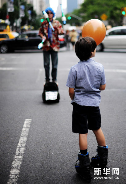 6月14日，在美國紐約曼哈頓第五大道，一名藝人的表演吸引了一個男孩駐足觀看。新華社記者申宏攝